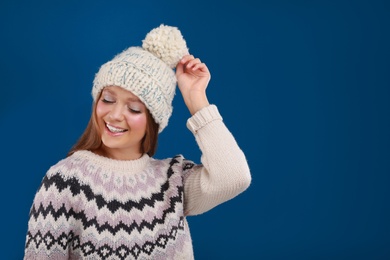 Photo of Young woman in warm sweater and hat on blue background, space for text. Winter season