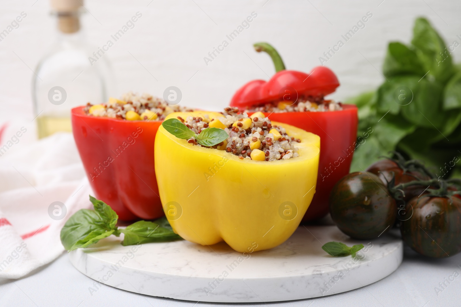 Photo of Quinoa stuffed bell peppers, basil and tomatoes on white table, closeup