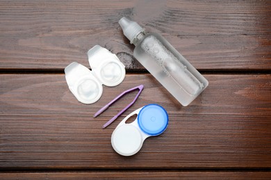 Photo of Packages with contact lenses, case, tweezers and drops on wooden table, flat lay