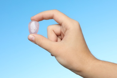 Woman holding beautiful pink quartz gemstone against blue background, closeup