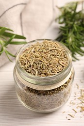 Glass jar with dry rosemary on white wooden table, closeup