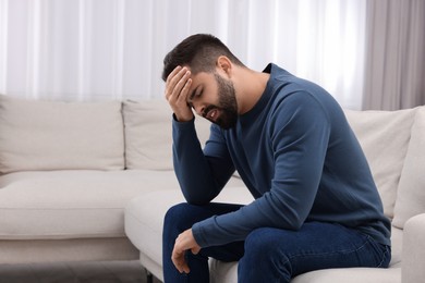 Photo of Man suffering from headache on sofa at home