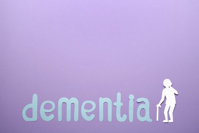 Photo of Word Dementia and old person paper cutout on violet background, flat lay. Space for text