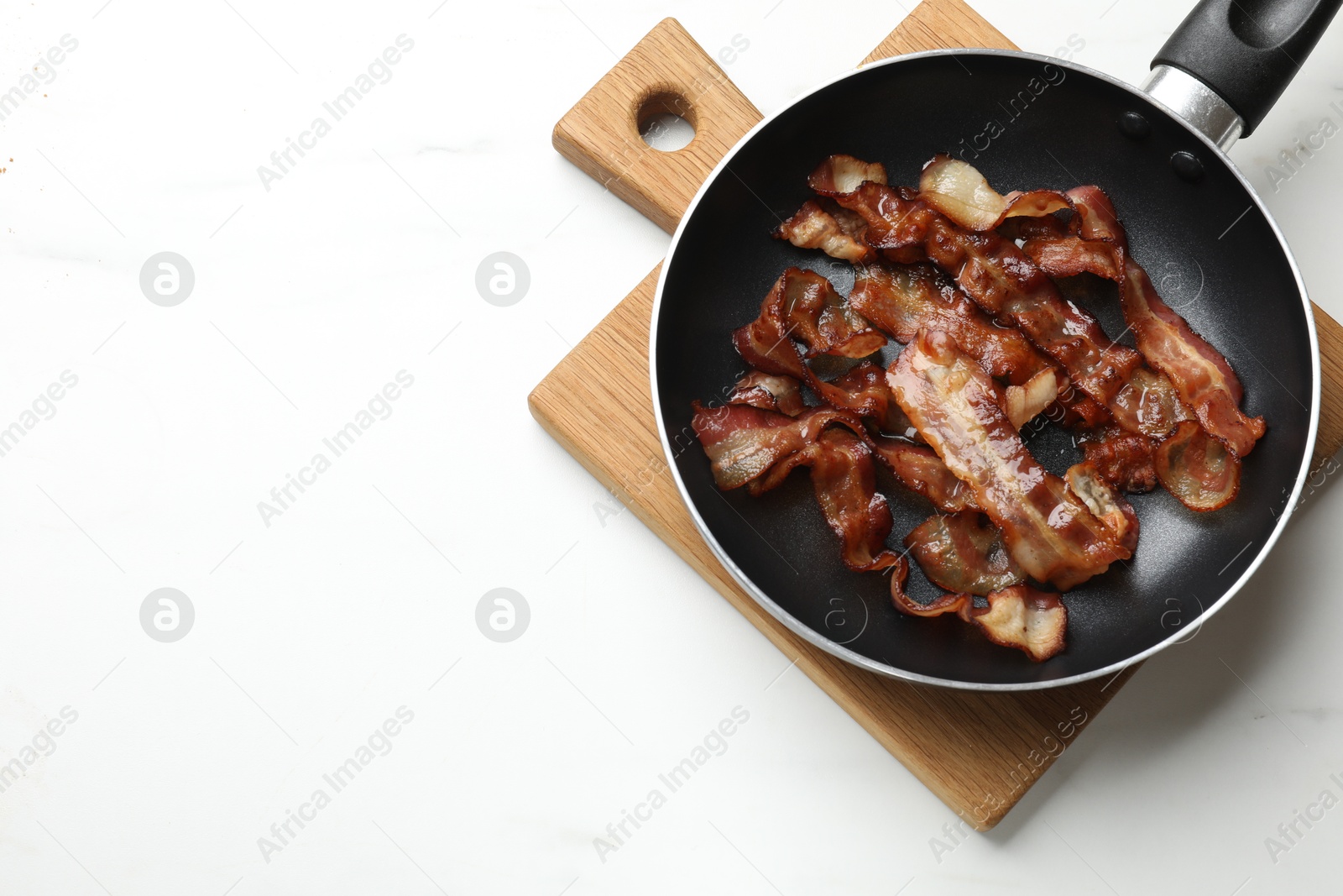 Photo of Delicious bacon slices in frying pan on white marble table, top view. Space for text