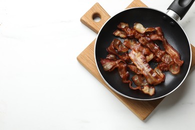 Photo of Delicious bacon slices in frying pan on white marble table, top view. Space for text