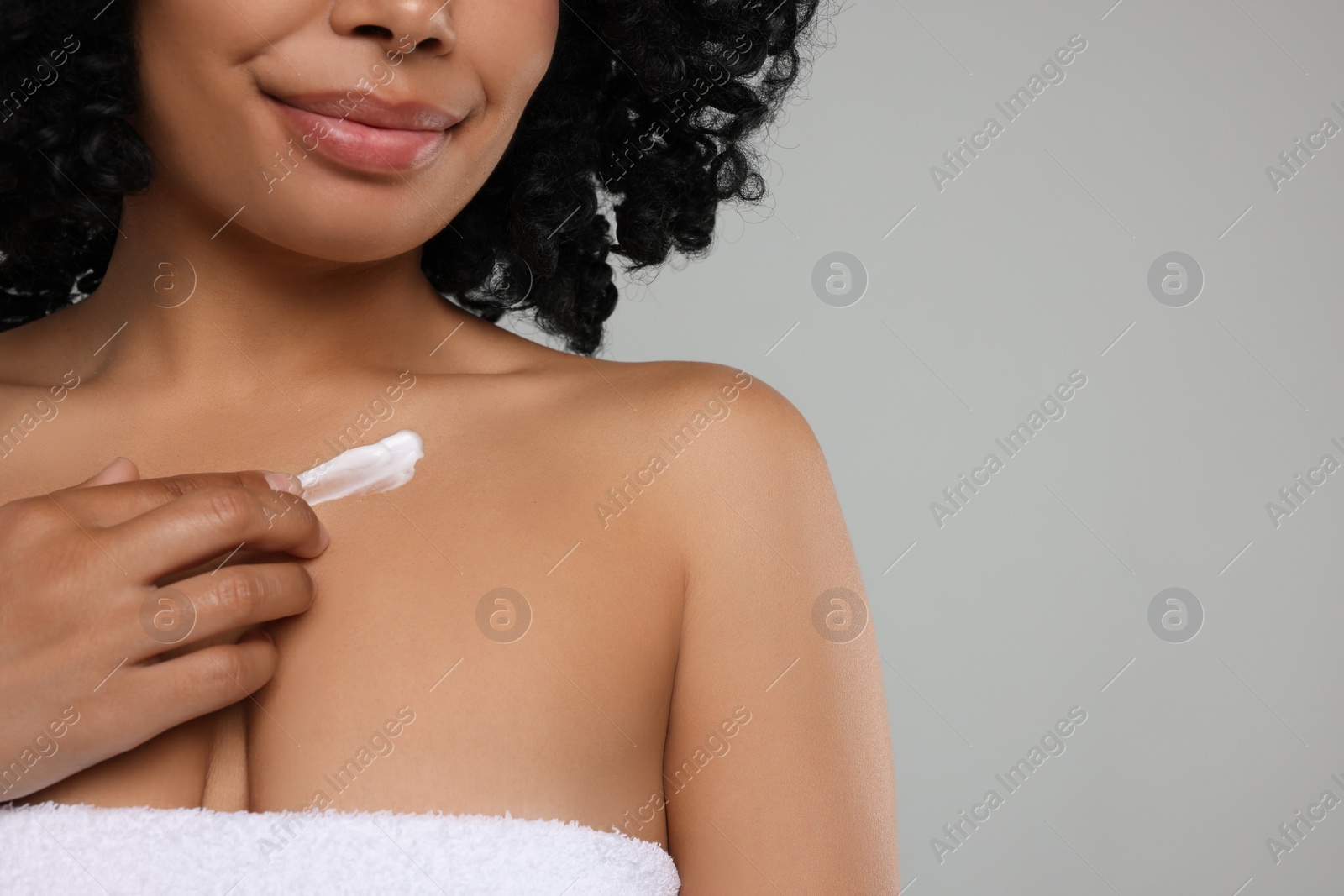 Photo of Young woman applying cream onto body on grey background, closeup. Space for text