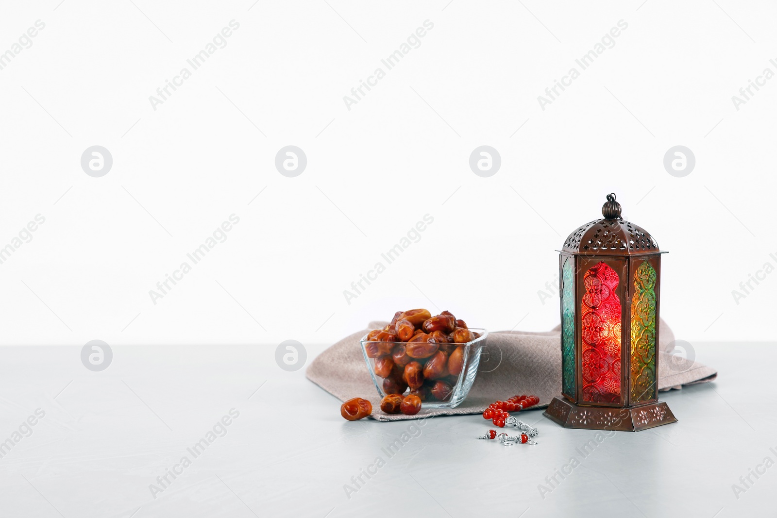 Photo of Muslim lamp, dates and prayer beads on table against white background. Space for text