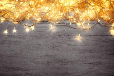 Photo of Glowing Christmas lights on white wooden background, top view. Space for text