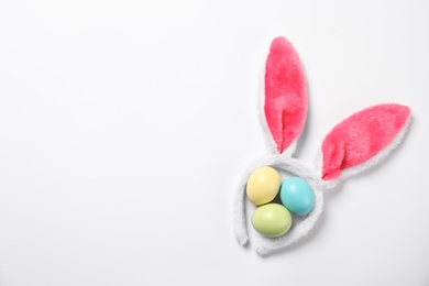 Photo of Funny headband with Easter bunny ears and dyed eggs white background, top view