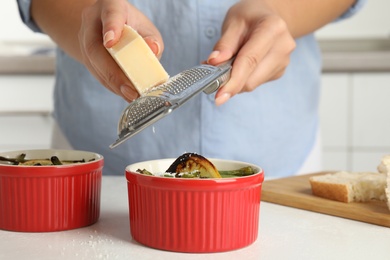 Photo of Woman grating cheese onto baked green beans at white table, closeup