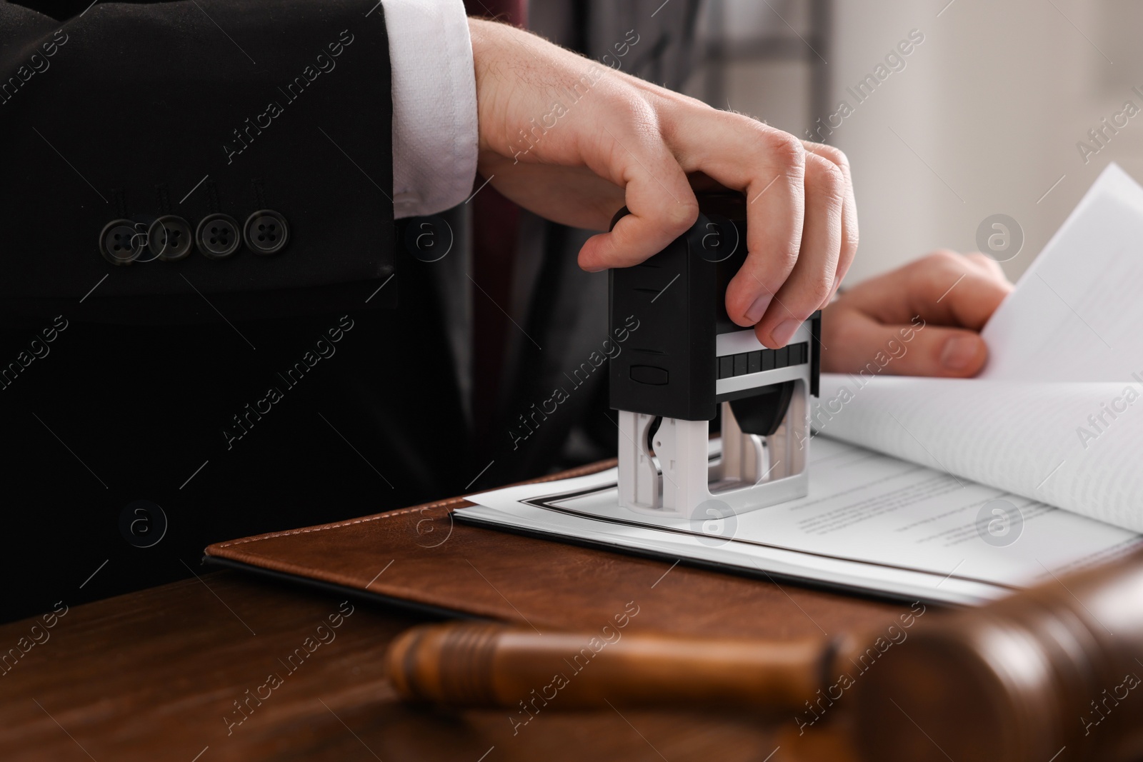 Photo of Notary stamping document at wooden table in office, closeup