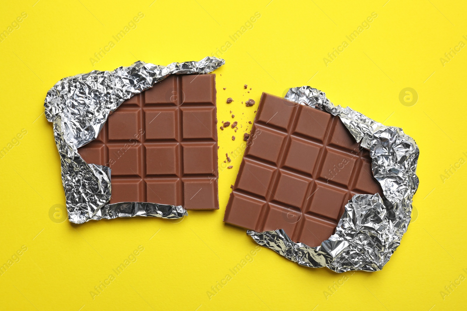 Photo of Parts of delicious chocolate bar on yellow background, flat lay