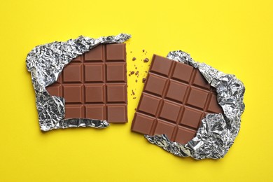 Photo of Parts of delicious chocolate bar on yellow background, flat lay