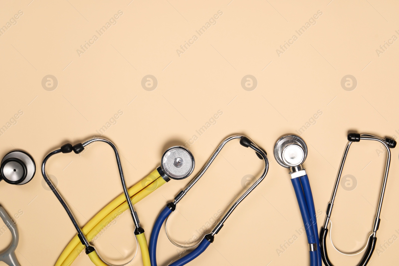 Photo of Stethoscopes on beige background, flat lay. Space for text