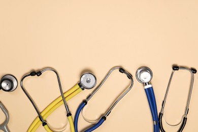 Stethoscopes on beige background, flat lay. Space for text