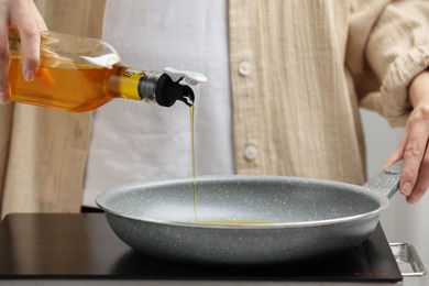 Photo of Vegetable fats. Woman pouring cooking oil into frying pan on stove, closeup