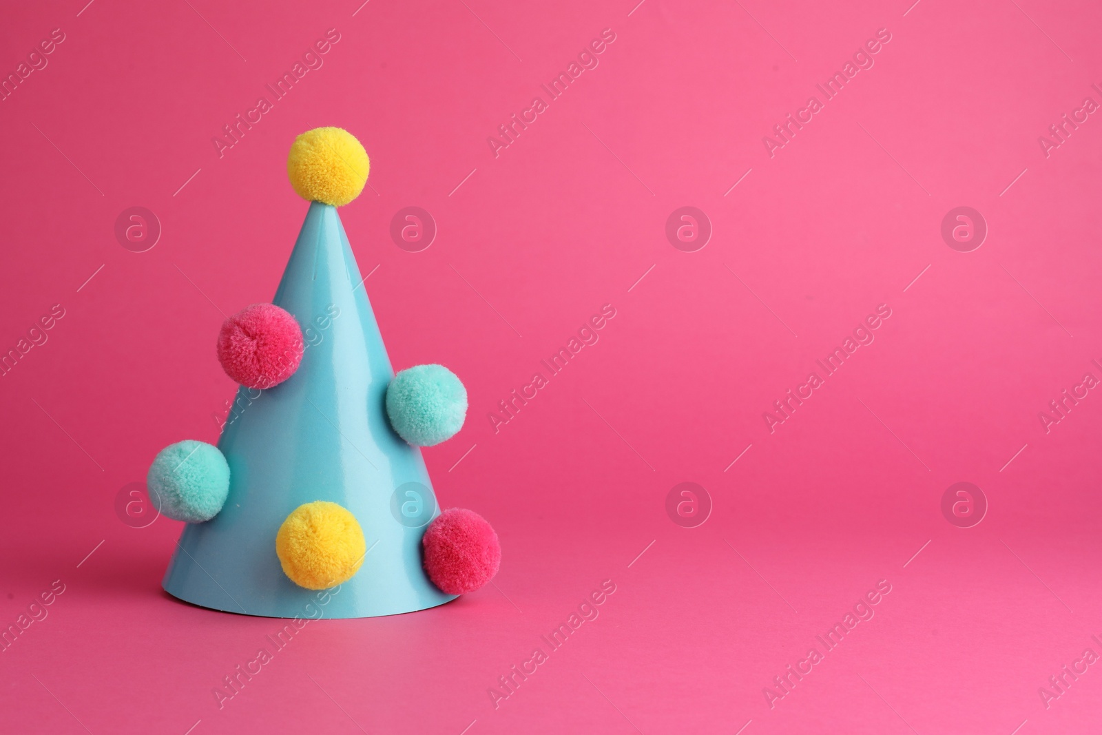 Photo of One light blue party hat with pompoms on pink background. Space for text