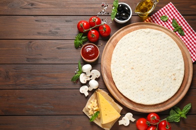 Flat lay composition with pizza crust and fresh ingredients on wooden table. Space for text