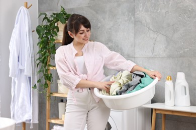 Happy young housewife holding basin with laundry in bathroom