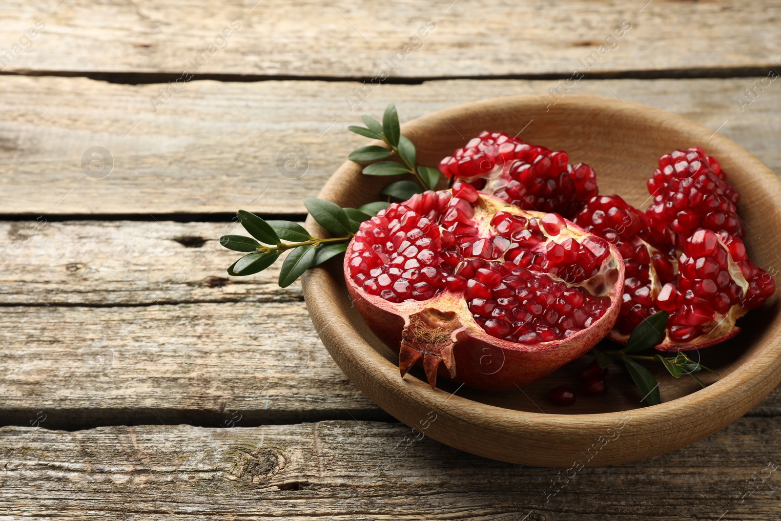 Photo of Cut fresh pomegranate and green leaves on wooden table, space for text