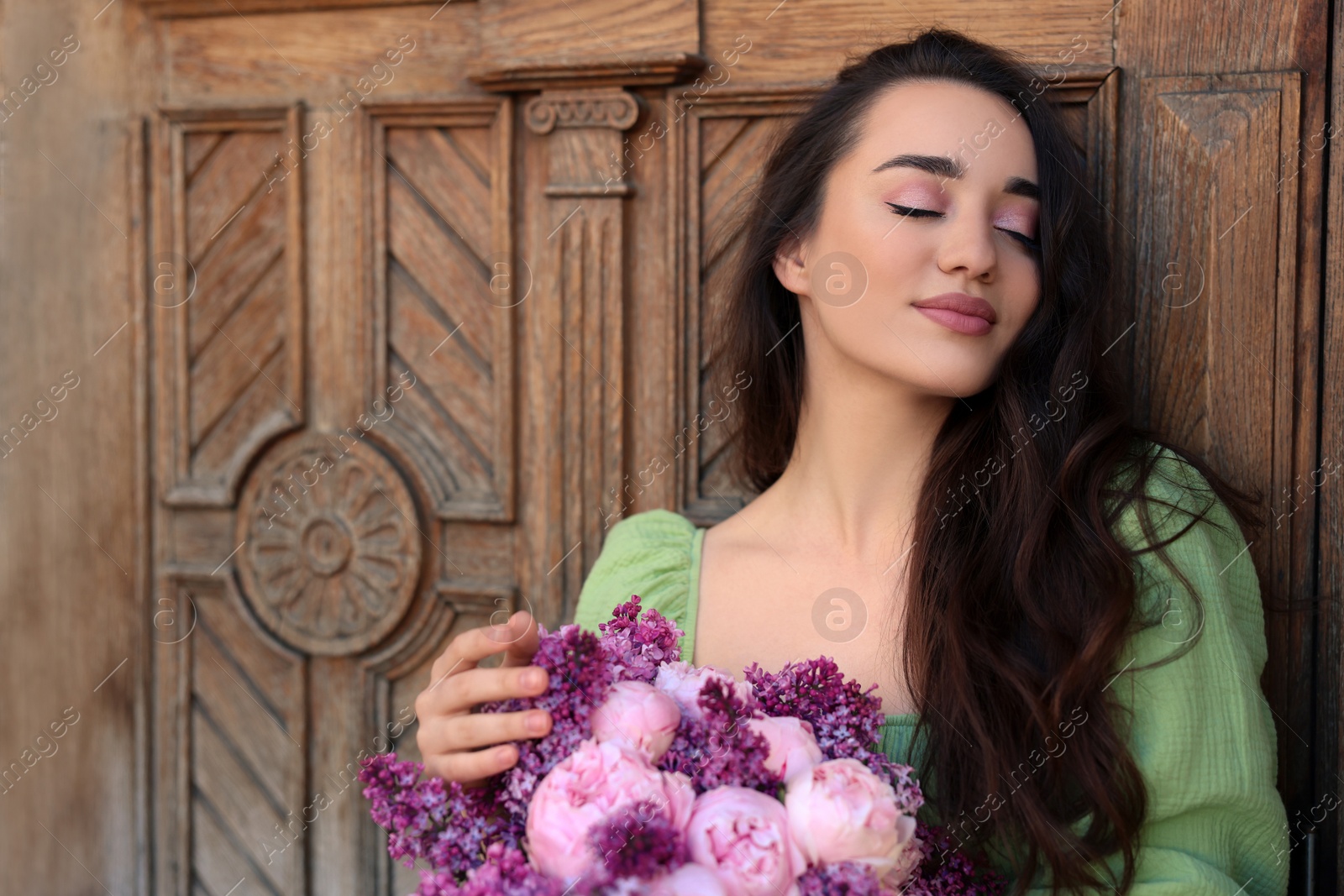 Photo of Beautiful woman with bouquet of spring flowers near wooden door, space for text