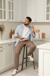 Photo of Handsome young man with notebook sitting on stool in kitchen