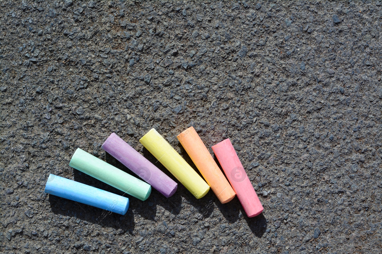 Photo of Colorful chalk sticks on asphalt, flat lay. Space for text