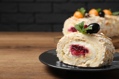 Photo of Slice of tasty meringue roll with jam, tangerine slices and mint leaves on wooden table, closeup. Space for text
