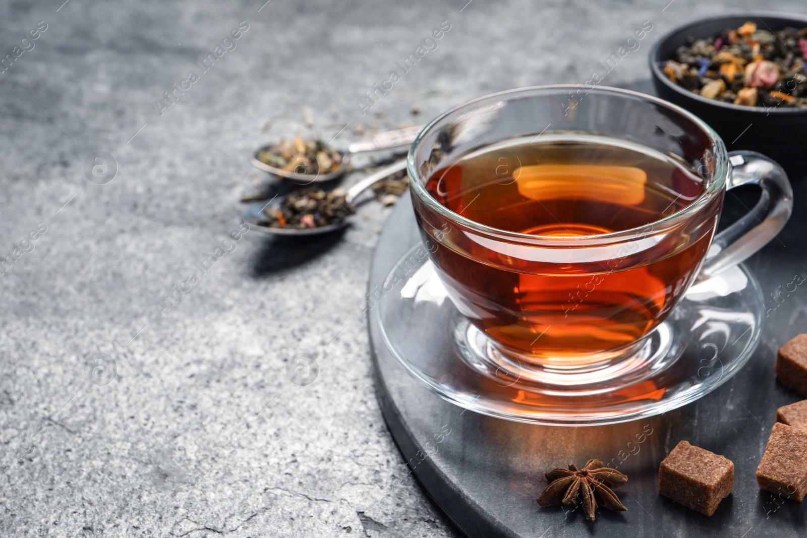 Photo of Glass cup of freshly brewed tea, dry leaves and sugar on grey table. Space for text