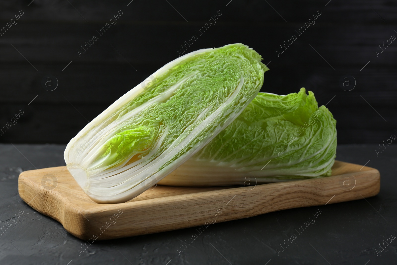 Photo of Whole and cut fresh Chinese cabbages on black textured table