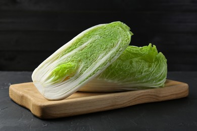 Photo of Whole and cut fresh Chinese cabbages on black textured table