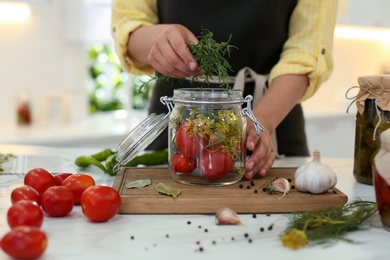 Woman putting rosemary into pickling jar at kitchen table, closeup