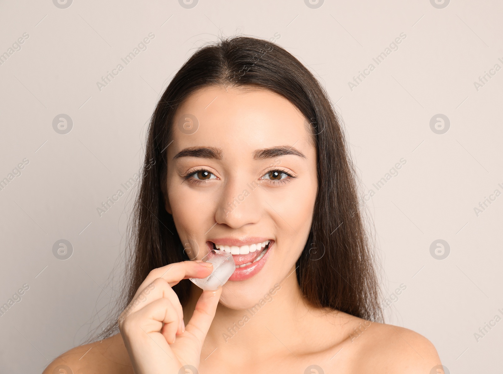 Photo of Young woman with ice cube on light background