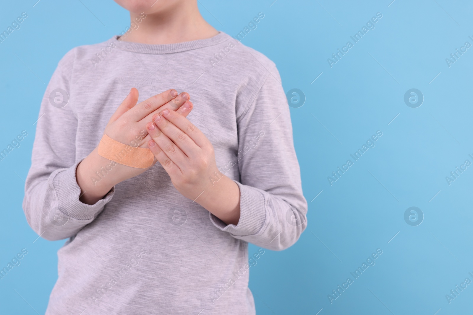 Photo of Little boy putting sticking plaster onto hand on light blue background, closeup. Space for text