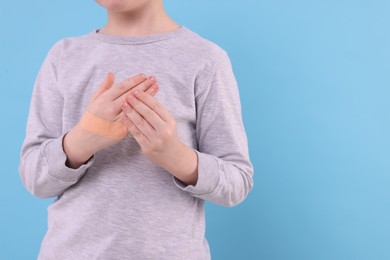 Little boy putting sticking plaster onto hand on light blue background, closeup. Space for text