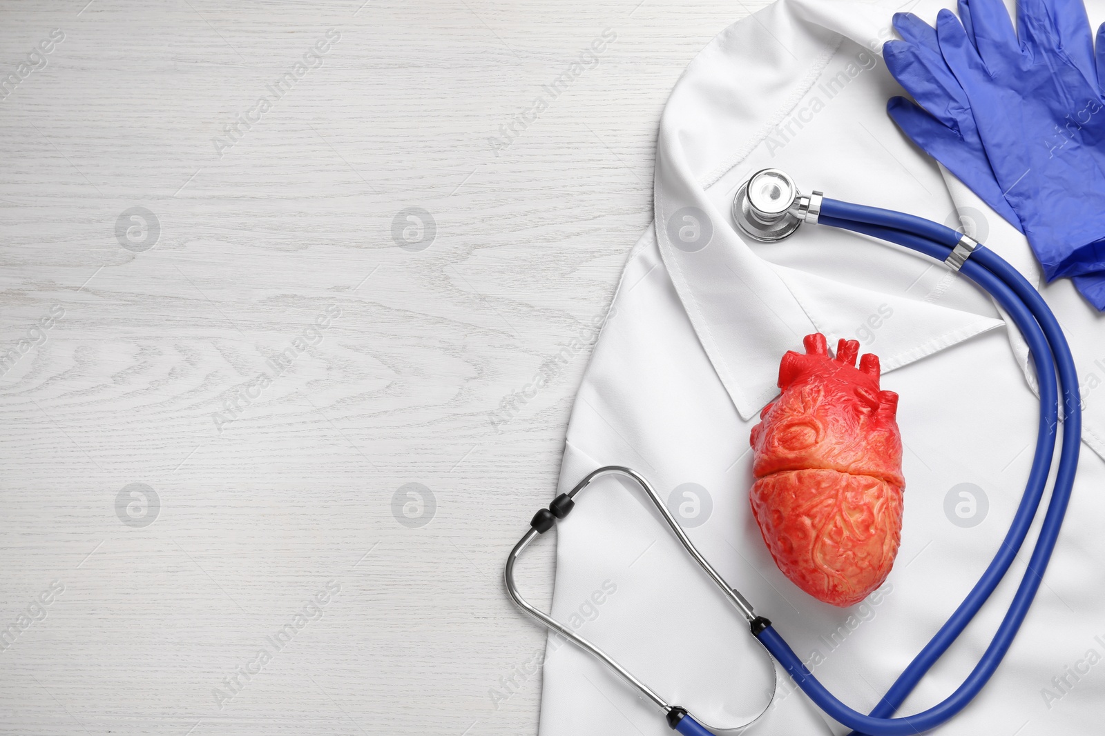 Photo of Flat lay composition with stethoscope and red heart model on white wooden table, space for text. Cardiology concept