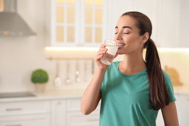 Photo of Young woman drinking pure water from glass in kitchen. Space for text
