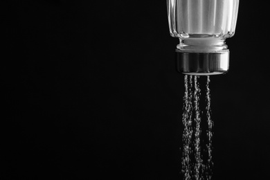 Photo of Pouring salt from shaker on black background, closeup. Space for text