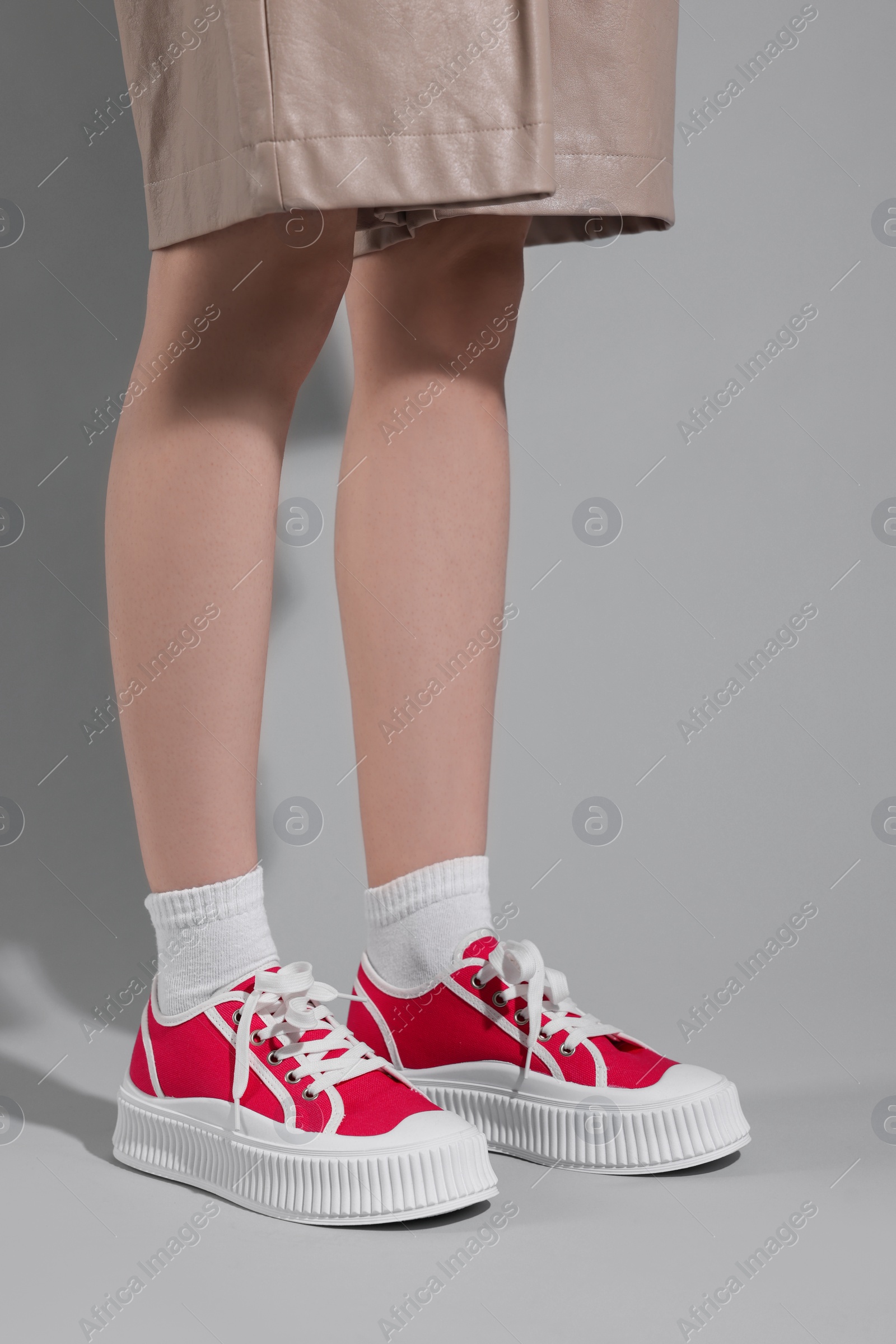 Photo of Woman wearing red classic old school sneakers on light gray background, closeup