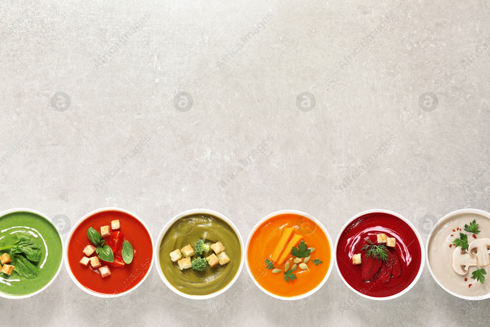 Photo of Various cream soups in bowls and space for text on grey background, top view