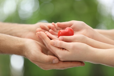 Photo of Parents and kid holding red heart in hands outdoors, closeup. Family day