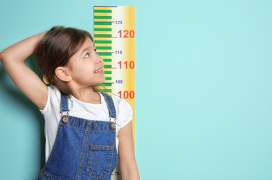 Photo of Little girl measuring her height on color background