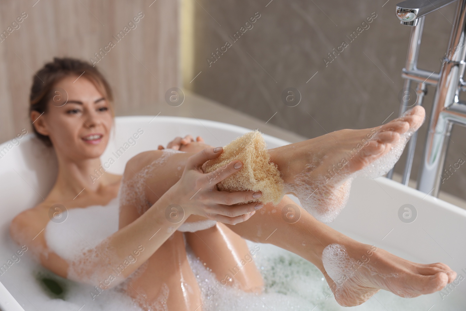 Photo of Beautiful woman with loofah taking bath indoors, focus on legs