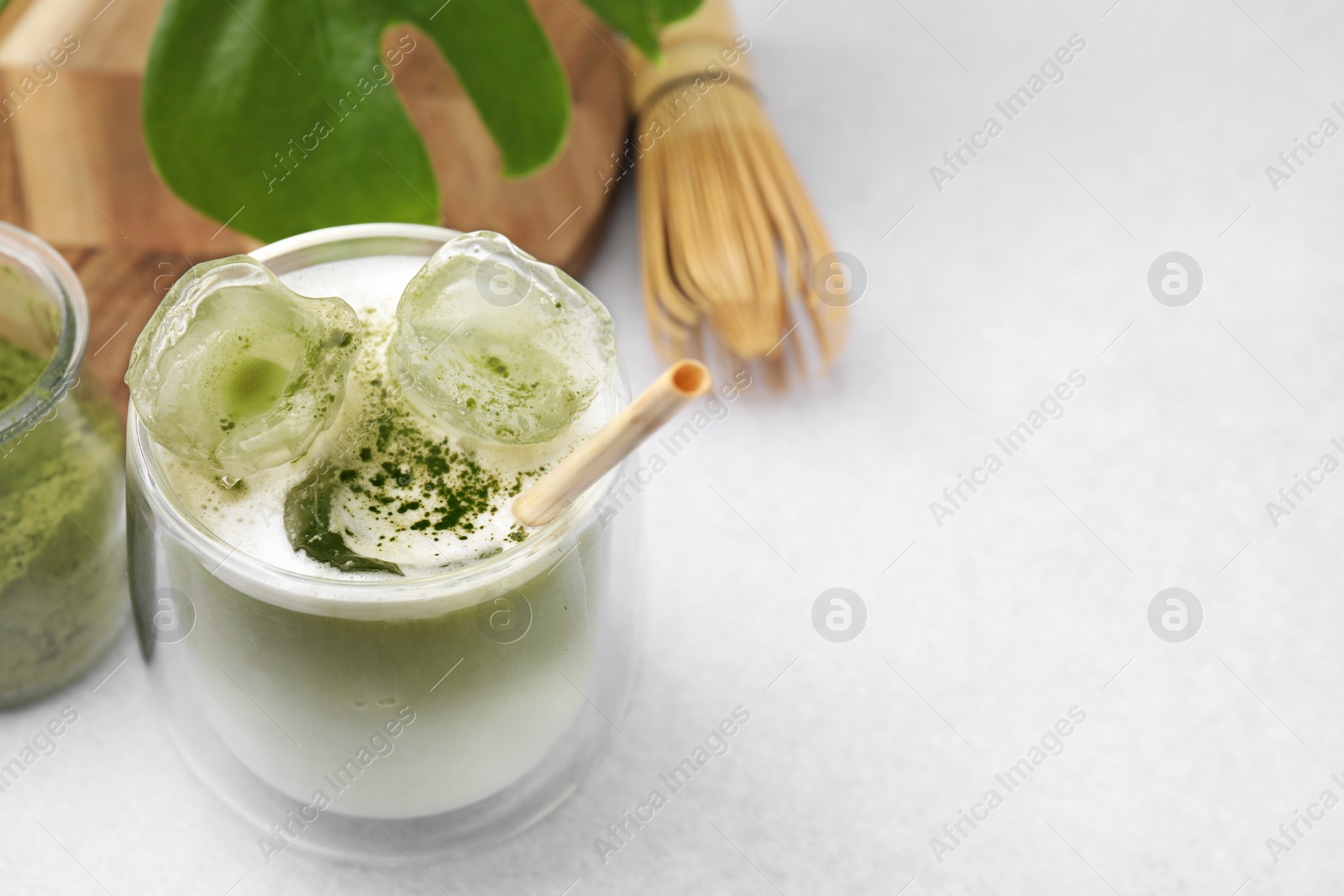 Photo of Glass of tasty iced matcha latte, leaf and bamboo whisk on white table, closeup. Space for text