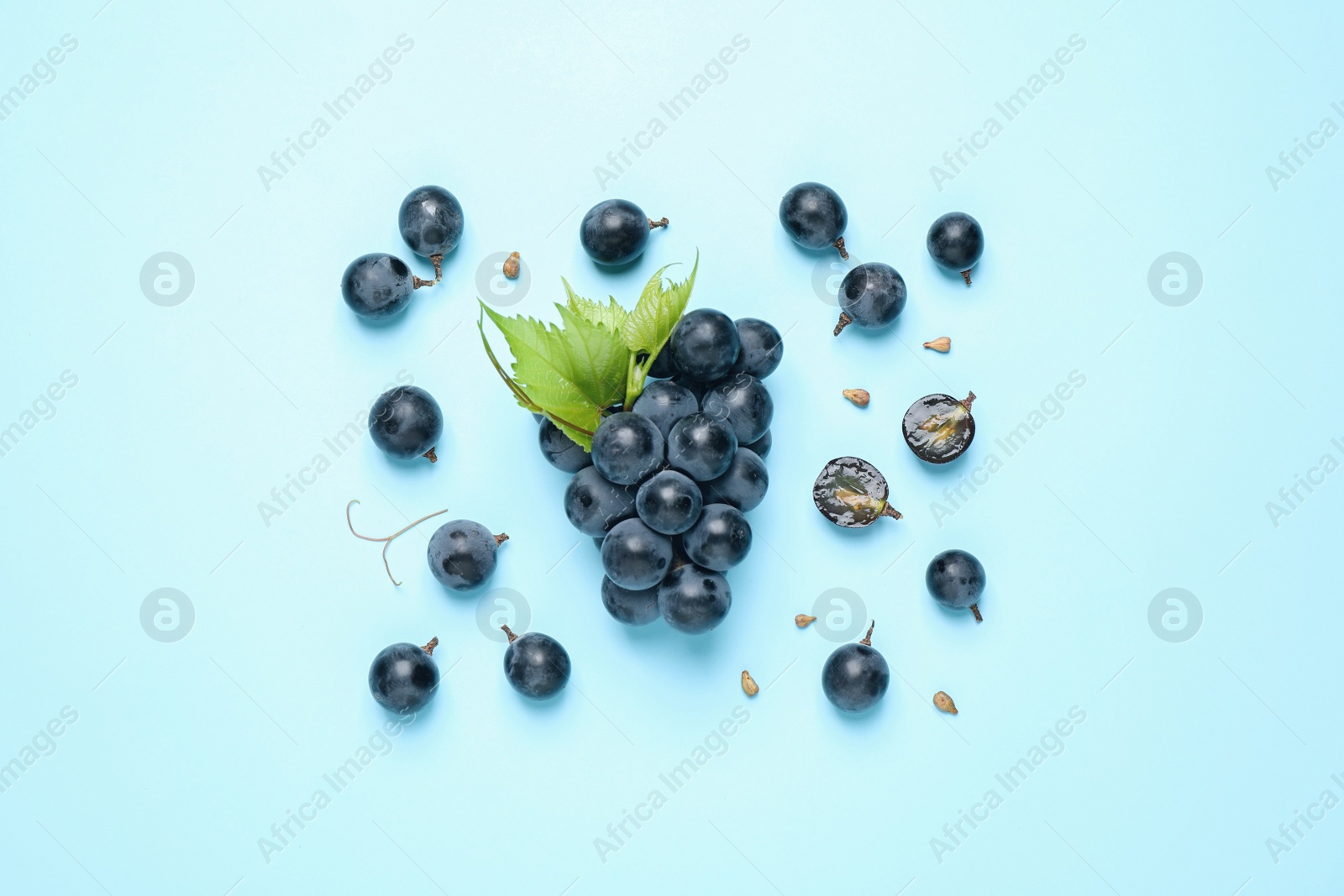 Photo of Bunch of ripe grapes with green leaves on light blue background, flat lay
