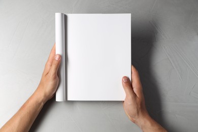 Photo of Man holding blank notebook at light grey table, top view. Mockup for design