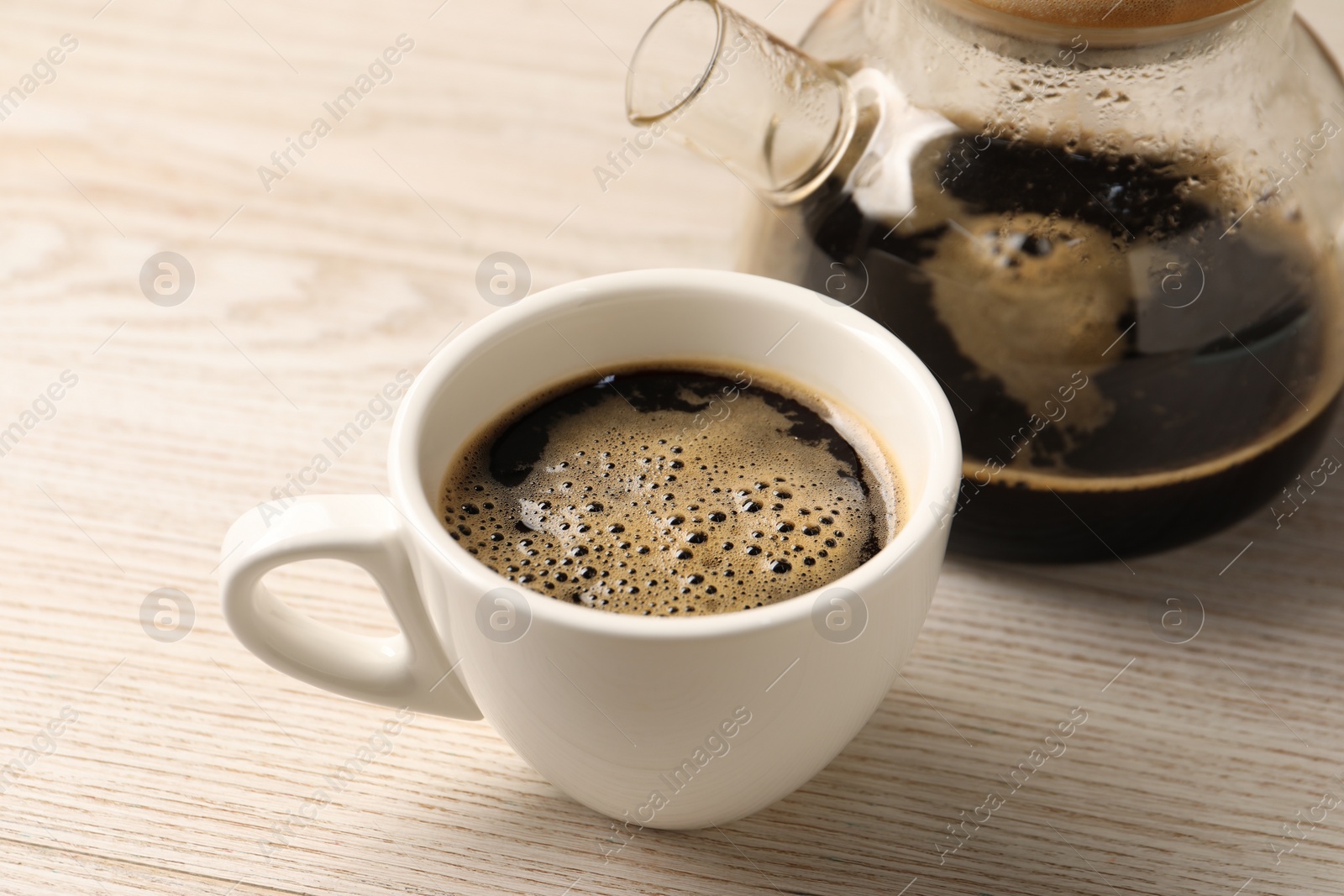 Photo of Aromatic coffee in cup and teapot on light wooden table, closeup