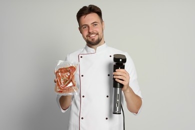 Photo of Smiling chef holding sous vide cooker and meat in vacuum pack on beige background