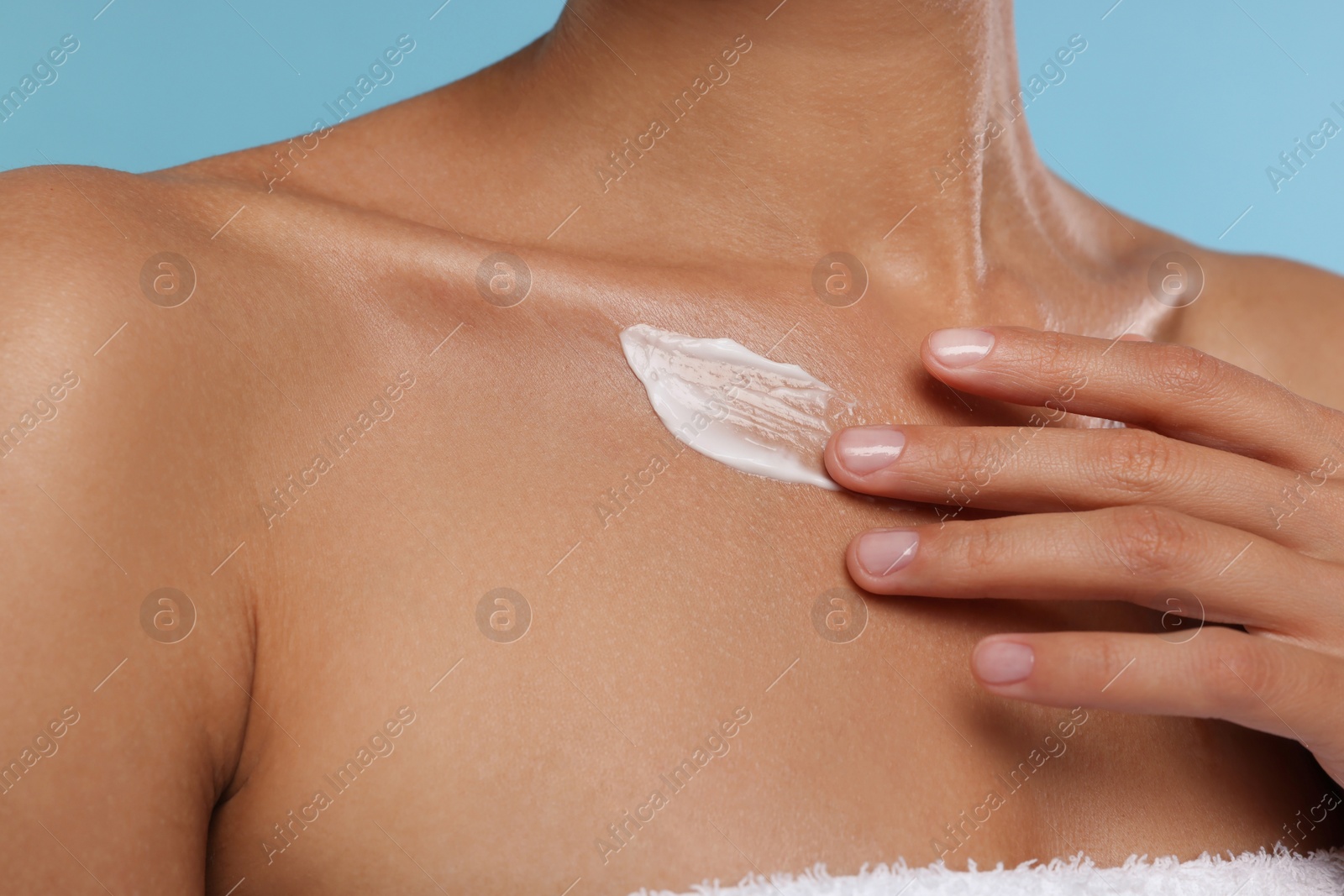 Photo of Woman applying cream onto body on light blue background, closeup