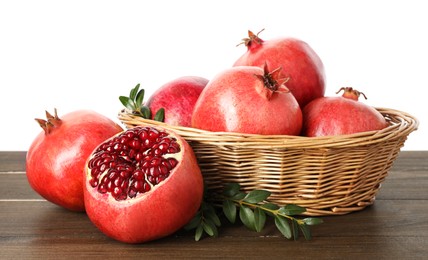 Fresh pomegranates in wicker basket and green leaves on wooden table against white background